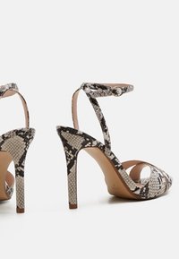 Paire de sandales à talons hauts avec brides autour de la cheville et motif serpent noir, blanc et gris, vues de profil sur fond blanc.