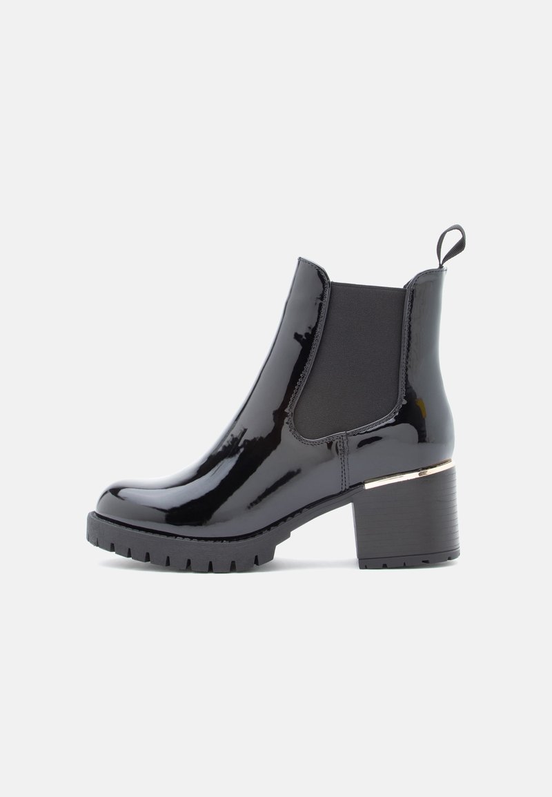 Bottine noire brillante à talon épais, panneaux latéraux élastiques, languette de tirage et semelle striée sur un fond clair uni.
