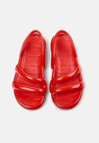 Red rubber sandals featuring a smooth texture, three wide straps, and a contoured footbed with small grooves for traction.