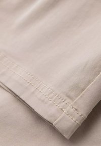 Tissu en coton beige avec une texture lisse, présentant un ourlet soigneusement cousu. Douces plis visibles, mettant en valeur le tombé et la finition du matériau.