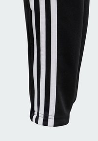 Zwarte sportbroek met drie witte verticale strepen langs de zijkanten, gemaakt van een zachte, gestructureerde stof met een tapering pasvorm.