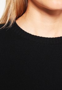 Maglione nero a costine con scollatura rotonda e superficie testurizzata, con dettagli di cucitura visibili lungo il colletto.