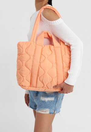 Sac cabas matelassé en tissu pêche doux, avec des motifs ondulés texturés, deux anses solides et une forme spacieuse et structurée.