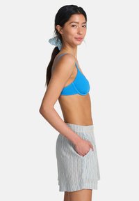 Soutien-gorge bleu texturé à fines bretelles associé à un short rayé clair avec cordon de serrage à la taille et poches latérales.