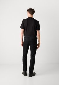 Zwarte t-shirt met korte mouwen, gecombineerd met zwarte slim-fit broeken. De broeken hebben achterzakken en worden gestyled met zwarte enkellaarzen.