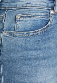 Calças de ganga azul claro com um design clássico, costuras visíveis, um pequeno bolso frontal e pormenores em metal.