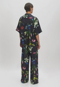 Blumenmuster weites Hemd und weite Hose aus dunkler Stoff, mit kräftigen Blumen in Rot-, Blau- und Grüntönen. Kurze Ärmel, entspannte Silhouette.