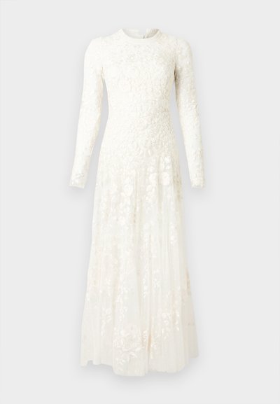 Λευκό μακρύ δαντελένιο φόρεμα με λουλουδάτα σχέδια, μακριά μανίκια, στενή κορυφή και ρέον πλισέ φούστα σε απλό φόντο.