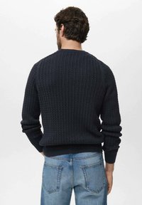 Suéter de punto en tono azul marino oscuro con un diseño texturizado y acanalado. Presenta un cuello redondo y puños ajustados. Se lleva con jeans de color azul claro.