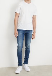 Vit rundhalsad T-shirt i kombination med ljusblå slim-fit jeans och vita sneakers. Slät tygtextur, standard passform och design.