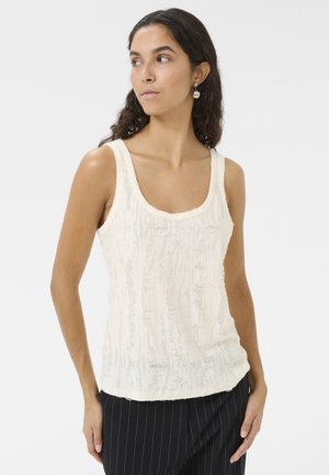 Cream-colored tank top with a textured, rippled design. Features a rounded neckline and is styled with black pinstripe trousers.