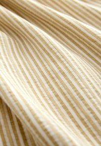 Primer plano de tela de rayas verticales beige y blanca con costuras visibles y pliegues suaves.