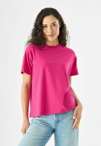 Fuchsia katoenen t-shirt met korte mouwen, ronde hals en een relaxte pasvorm. Heeft minimale branding op de borst. Draagt bij lichte blauwe jeans.