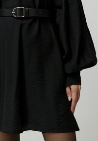 Zwarte gestructureerde jurk met een bijpassende riem in de taille. Lange, volumineuze mouwen en een licht uitlopende zoom, gemaakt van lichte stof.