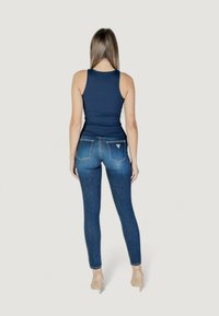Marineblauwe tanktop gecombineerd met aansluitende blauwe spijkerbroeken. De spijkerbroeken hebben twee achterzakken en subtiele stiksels langs de naden.