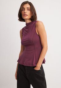 Fioletowa, bezrękawnikowa bluzka z drapowanym dekoltem i peplum, wykonana z gładkiego materiału; zestawiona z czarnymi spodniami, minimalistyczny design.