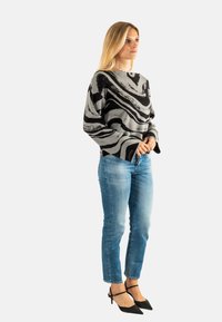 Grijze trui met zwarte draaiende patronen, lange mouwen, relaxte pasvorm. Gecombineerd met lichtblauwe jeans en zwarte puntige hakken.