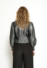 Glanzend grijs cropped blouse met puffed mouwen, textuurstof en aansluitende manchetten, gecombineerd met hooggerokte zwarte broek.