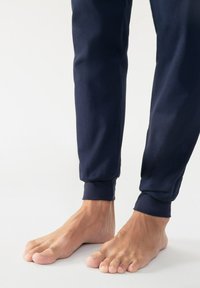 Navy blauwe joggingbroek met ribgebreide boorden. Zachte stof, taps toelopende pasvorm. Blote voeten zichtbaar onderaan, wat de natuurlijke huidstructuur toont.