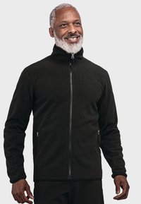 Schwarze Zip-Jacke mit einem strukturierten Muster, hohem Kragen und Seitentaschen. Hergestellt aus einem weichen Material, mit einem subtilen Logo auf der Brust.