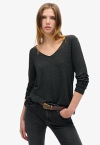 Zwarte langmouwen V-hals top met een zachte textuur, gecombineerd met donkere jeans en een bruine riem. Heeft een ontspannen pasvorm en licht gerimpelde mouwen.