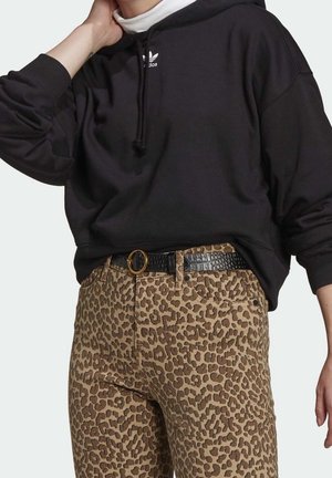 Persoon draagt een zwarte Adidas-hoodie en hooggetailleerde broek met luipaardprint, met een zwarte riem met een ronde gouden gesp.