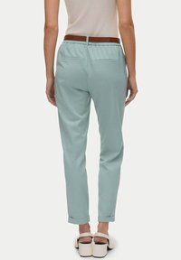 Pantaloni azzurri chiari, a sigaretta, con vita elastica, tasche posteriori e orli arrotolati, abbinati a una cintura marrone e calzature bianche.