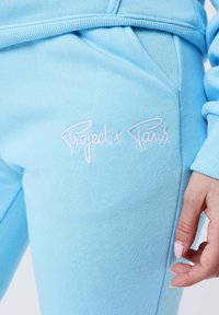 Lyseblå bomulds tracksuit med en sidelomme. Har et broderet pink logo "Project x Paris" på låret. Glat tekstur, afslappet pasform.