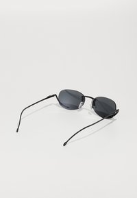 Ochelari de soare black metal cu lentile gri, formă ovală, brațe subțiri și tampoane de nas transparente. Design minimalist, textură netedă.