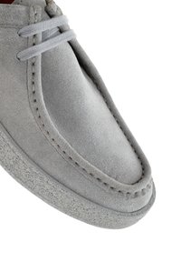 Zapato de ante gris con puntera redondeada, costuras decorativas y suela de goma texturizada. Incluye cordones grises para un ajuste seguro.