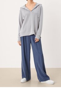 Sudadera con capucha de color gris claro y escote en V; combinada con pantalones anchos de pierna ancha en azul y zapatillas blancas. Presenta una tela suave y mangas largas.