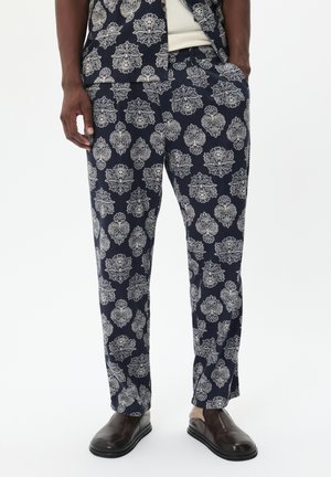 Navy pants with a white floral pattern, crafted from lightweight fabric. Features an elastic waistband and side pockets, paired with dark slip-on shoes.