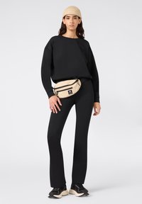 Felpa nera e leggings abbinati a una borsa a vita beige. Tessuto morbido, vestibilità comoda, e sneakers nere completano l'outfit.
