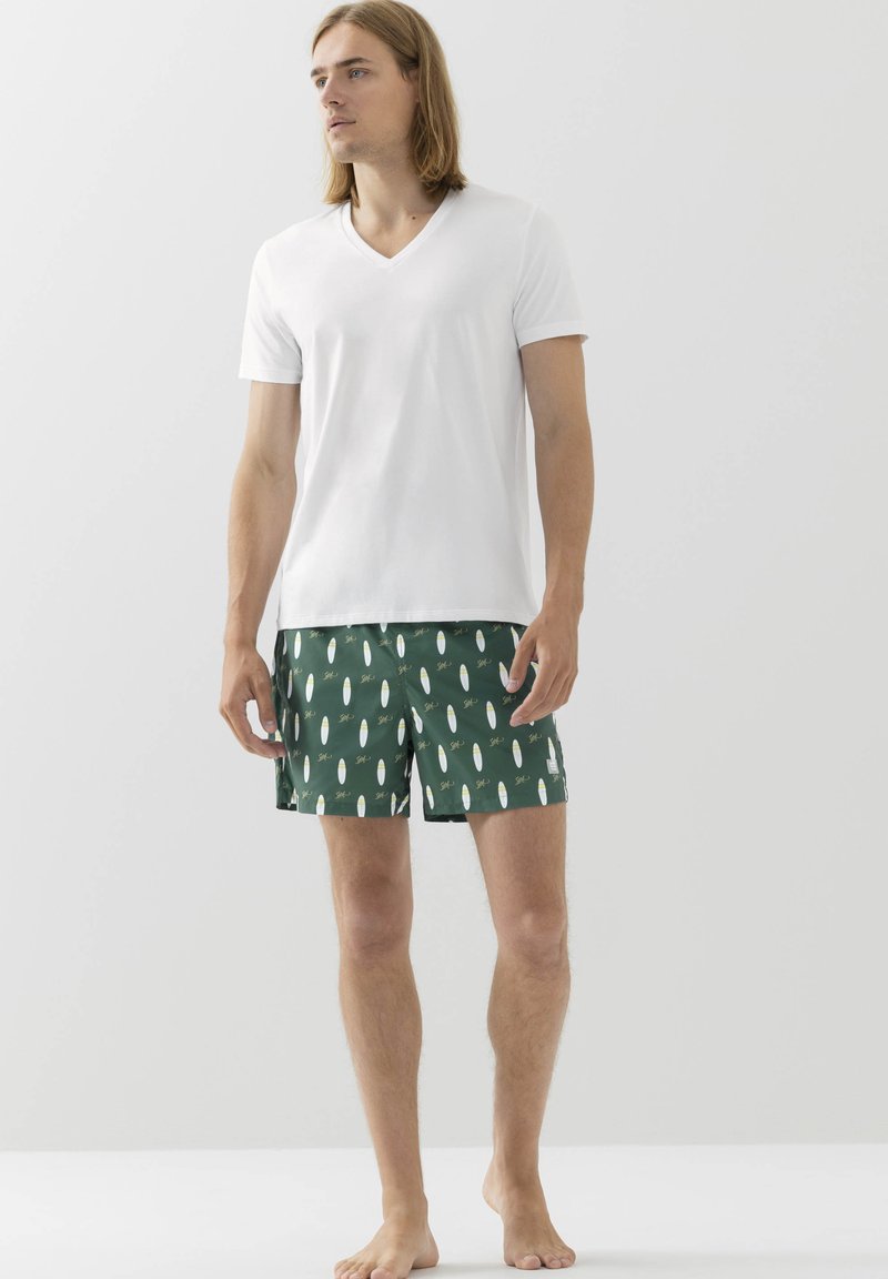 Bílý tričko s výstřihem do V v kombinaci se zelenými plavkami s potiskem surfboardu. Lehká tkanina, krátké rukávy a elastický pas.