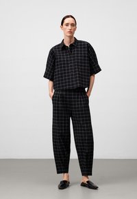 Zwart-wit geblokte cropped shirt met een kraag, gecombineerd met zwart-wit geblokte loszittende broek en zwarte instappers.