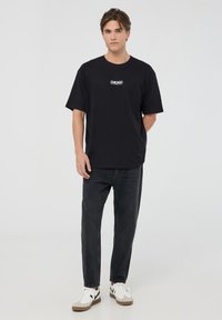 T-shirt nera in cotone a maniche corte, con testo bianco "CHICAGO". Abbinata a jeans di denim scuri e sneakers bianche con dettagli neri.