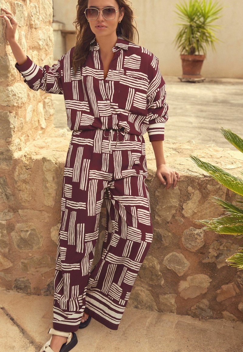 Ensemble deux pièces bordeaux avec des motifs à rayures blanches. Comprend une chemise à col et un pantalon large, fabriqués dans un tissu léger.
