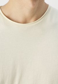 Short-sleeve, light beige t-shirt with a round neckline. Soft, smooth texture with a slight stretch. Minimalist design, no visible patterns or accents.