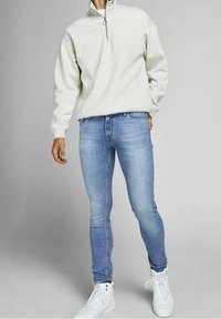 Light gray zip-neck sweatshirt with long sleeves paired with blue slim-fit jeans and white high-top sneakers. Smooth fabric texture.