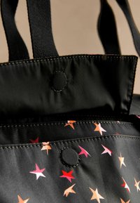 Zwarte stoffen draagtas met een kleurrijk sterrenpatroon in roze, rood en oranje. Voorzien van zwarte handvatten en een drukknoopsluiting.
