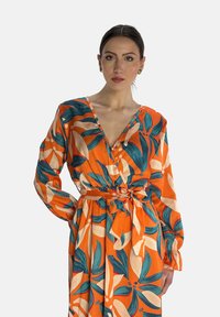 Robe florale orange avec un décolleté en V profond, des manches longues, une taille cintrée avec un lien, et un motif de feuilles vibrant en bleu canard et crème.