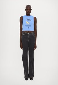Nebesky modrý crop top s potlačeným textom a grafikou stoličky; skombinovaný s vysokými tmavomodrými rozšírenými džínsami.