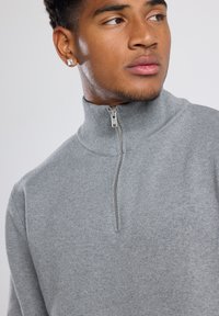 Gray zip-up pullover sweater made of a textured knit fabric. Features a high collar and a silver zipper at the front.