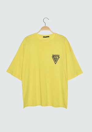 Gelbes oversized T-Shirt mit kurzen Ärmeln, das an einem Holzbügel hängt, mit schwarzem "California LA" Dreieckslogo auf der linken Brust.