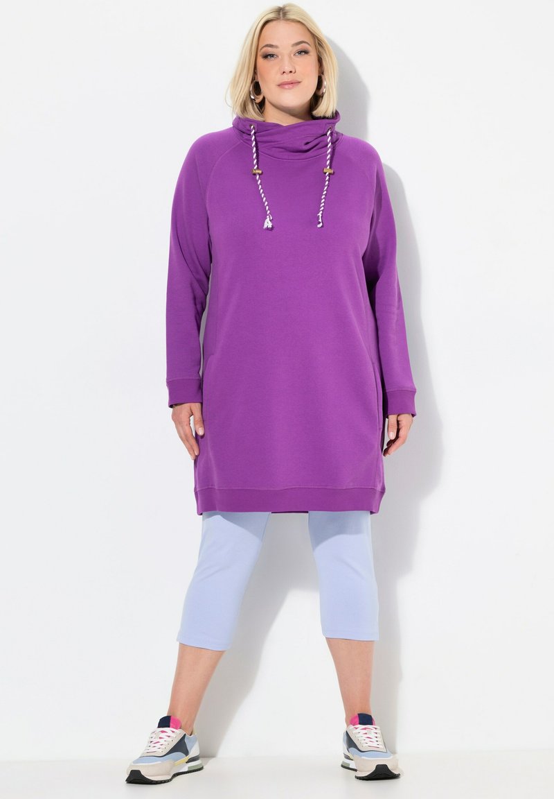 Lila Kapuzen-Tunika mit Kordelzug, lockere Passform, kombiniert mit hellblauen Capri-Leggings und Sportschuhen, die graue, weiße und rosa Akzente aufweisen.
