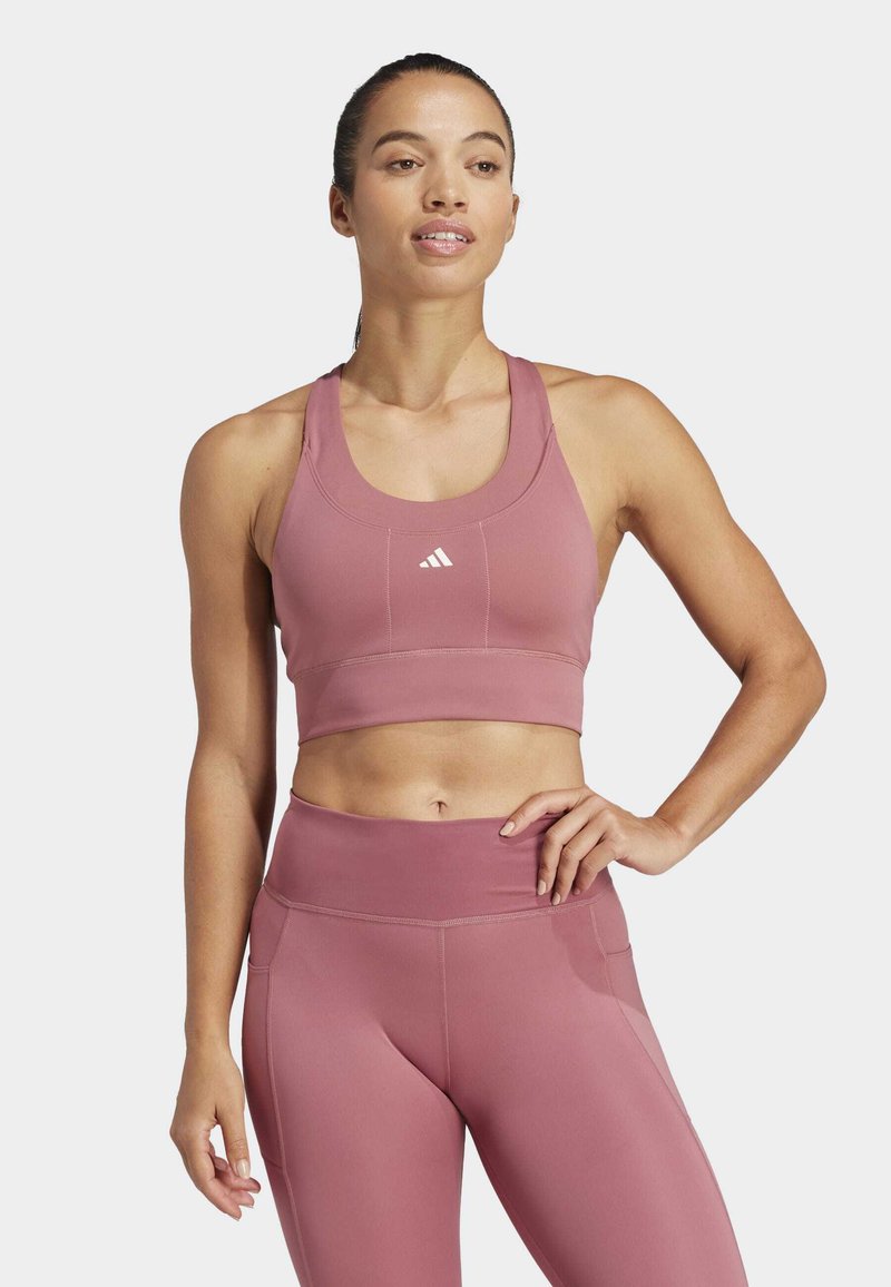 Top deportivo rosa de corte crop con escote redondo y tirantes anchos, combinado con leggings de cintura alta. Presenta una textura suave y un mínimo de marcas.