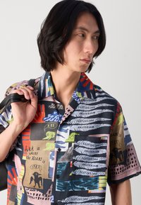 Short-sleeve, button-up shirt made of fabric featuring a colorful collage of patterns, graphics, and text in various colors, primarily navy and pastel shades.