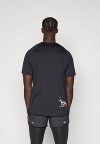 Fekete, rövid ujjú sportpóló ívelt aljjal, halmintával és szöveggel a hátsó alsó részen, valamint raglán ujjak.