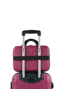 Maleta rígida rosa con una textura suave, asa plateada retráctil y una bolsa más pequeña asegurada en la parte superior con una correa negra.