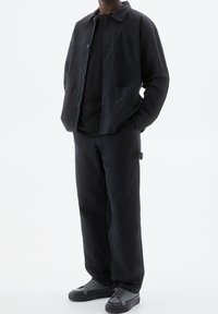 Black jacket with a collar and front buttons, paired with a black t-shirt and black wide-leg pants. Sneakers feature gray accents.